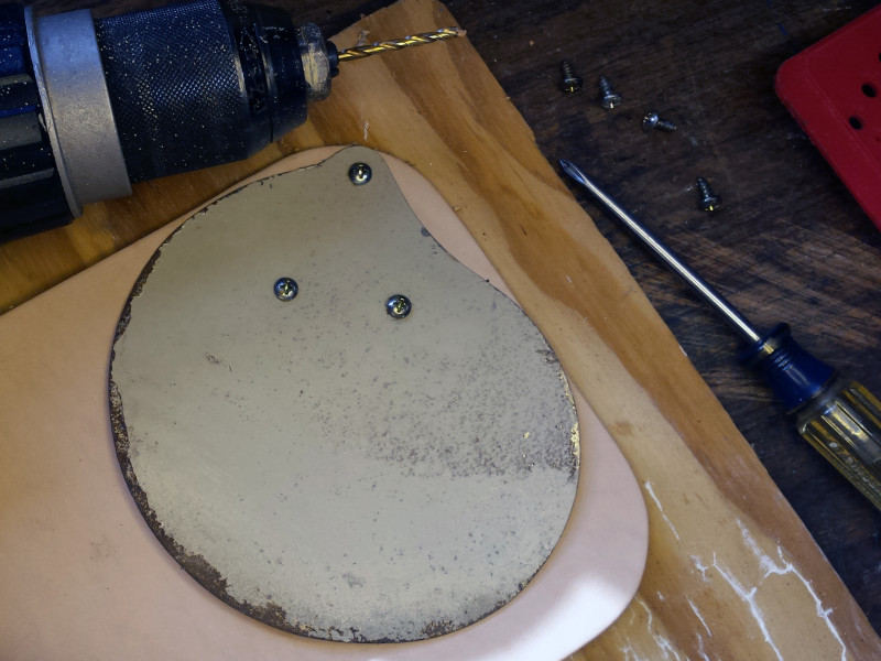 1. Put a piece of scrap wood down on your work surface, and then put your leather stock on top of that. Top the stack off with the template fan blade, then drill pilot holes through the blade mounting holes, through the leather, and into the wood. Secure the blade and leather to the wood with three small wood screws.